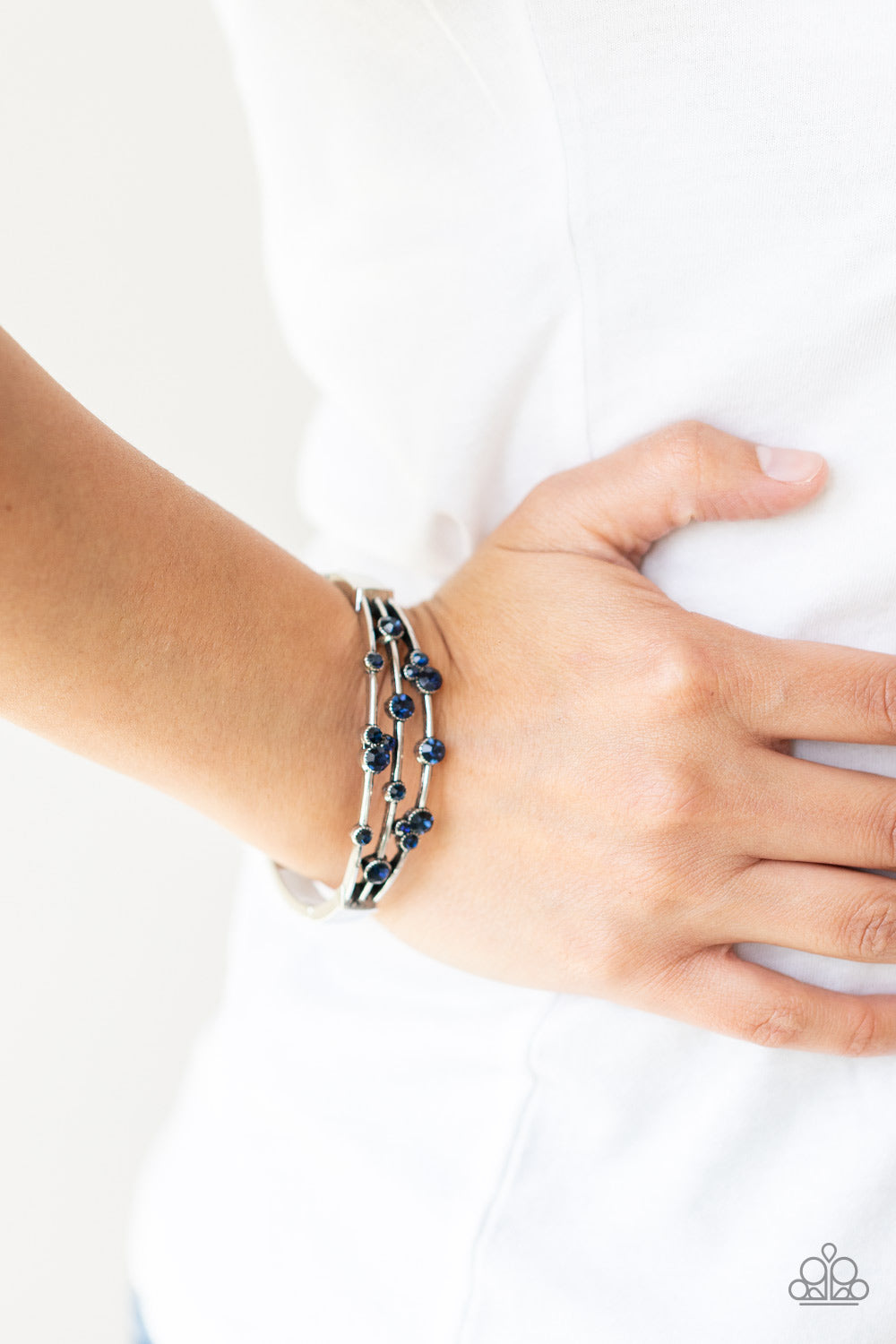 A smattering of glittery blue rhinestones adorn three silver bars that coalesce into a versatile silver cuff-like bangle around the wrist. Features a hinged closure.  Sold as one individual bracelet.