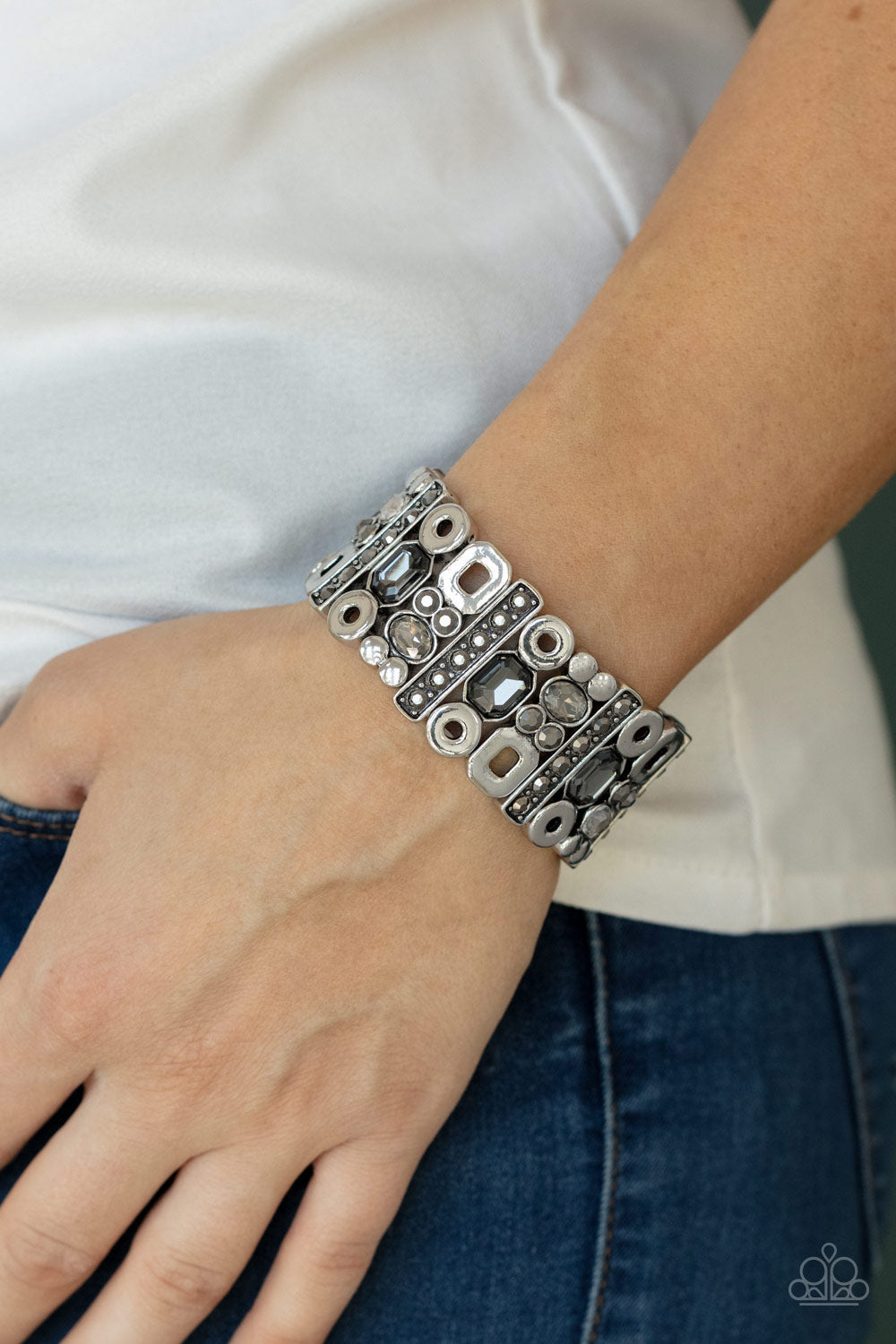 Infused with flat silver studs and geometric silver accents, a mismatched assortment of oval, round, and emerald style hematite and smoky rhinestones coalesce into edgy frames along a stretchy band for an intense sparkle around the wrist.  Sold as one individual bracelet.