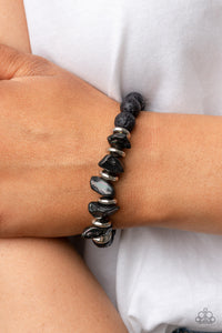 An earthy collection of black lava rock beads, dainty silver discs, and black oil spill metallic pebbles are threaded along a stretchy band around the wrist, resulting in an edgy look. Due to its prismatic palette, color may vary.  Sold as one individual bracelet.