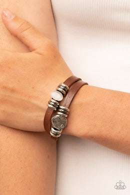 Infused with trios of silver and gunmetal rings, a glassy silver cat's eye stone and hammered silver disc stamped in a starry sun and moon pattern adorns layered brown leather bands around the wrist for a seasonal fashion. Features an adjustable snap closure.  Sold as one individual bracelet.